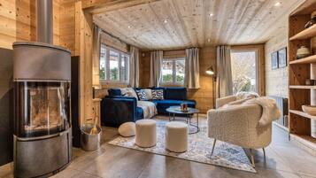 L’intérieur d’un chalet confortable, avec un poêle à bois, un canapé bleu, un fauteuil beige et une petite table.