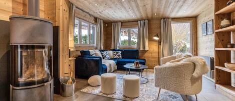 L’intérieur d’un chalet confortable, avec un poêle à bois, un canapé bleu, un fauteuil beige et une petite table.