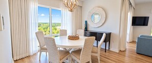 A dining area with a round table, wicker chairs, a chandelier, a sideboard, and a television on the wall. - Luau II 6622-6624LO, New to Rentals, Pool Views, (Miramar Beach)