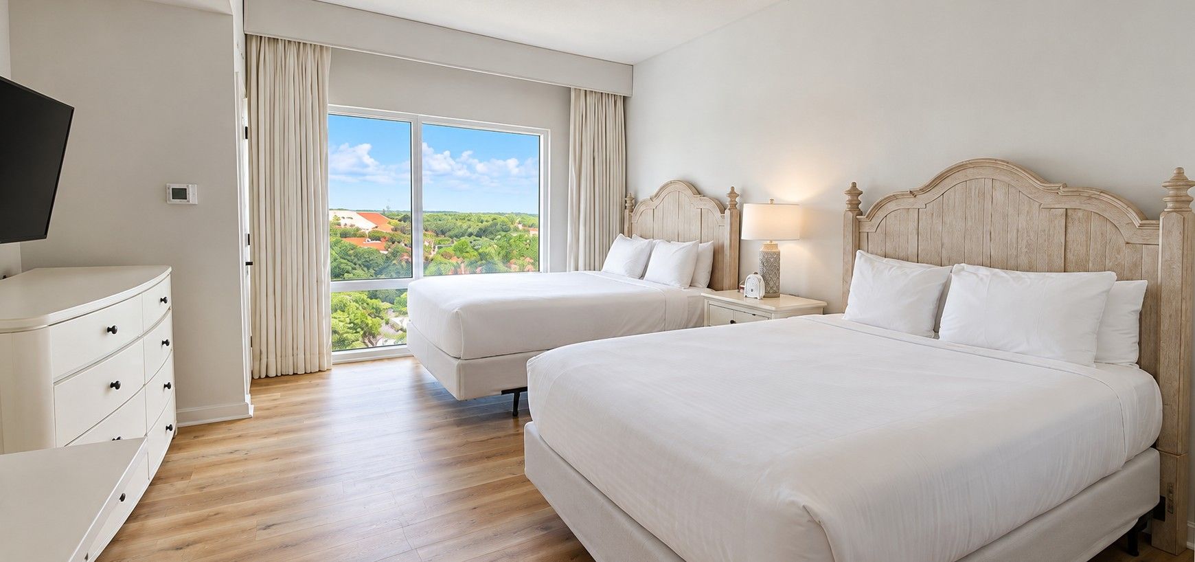Een hotelkamer met twee bedden, een televisie, een dressoir en een groot raam met uitzicht op het landschap.