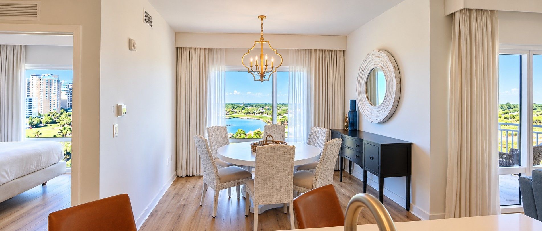 A hotel room with a dining area, a bed, a view of the city, and a large window.