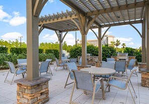 Ein Außenbereich mit Terrasse, Tischen, Stühlen, einer Pergola und einem Kamin aus Stein.