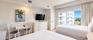 Quarto de hotel com cama, escrivaninha, cadeira, televisão e um quadro.