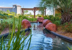 Un élément décoratif aquatique agrémenté de rochers et d’une pergola, intégré dans un jardin aménagé.