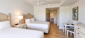 A hotel room with two beds, a desk, a chair, a painting, and a ceiling fan. - New to Rental Program | Luau Lagoon Hideaway | Two Queen Beds (Miramar Beach)