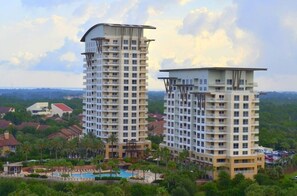 A high-rise hotel with multiple floors, a swimming pool, and a lush green landscape in the background. - New to Rental Program | Luau Lagoon Hideaway | Two Queen Beds (Miramar Beach)