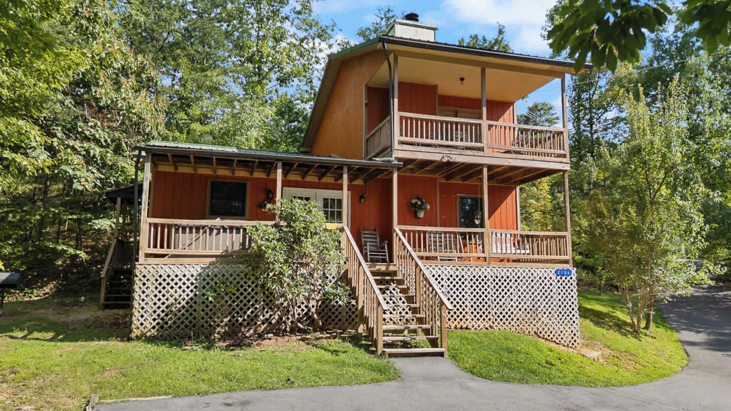 Eine zweistöckige Hütte mit einem Balkon, Holzgeländern und einem umzäunten Garten.