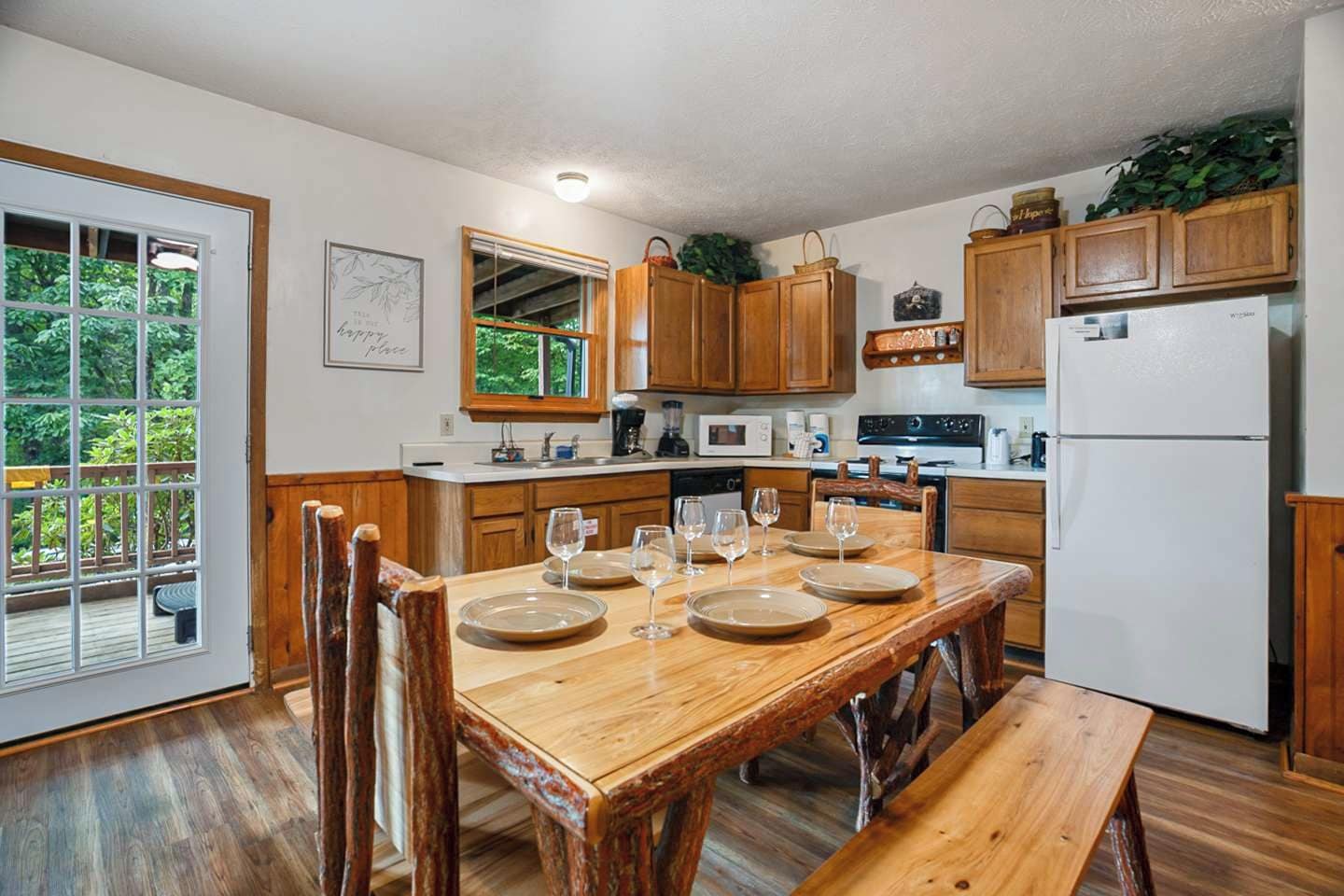 A kitchen with wooden cabinets, a dining table set with plates and glasses, and a refrigerator.