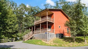 Eine zweistöckige Holzblockhütte mit einem Balkon, umgeben von Bäumen.