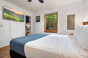 Ein Schlafzimmer mit einem Bett, einem Kleiderschrank, einem Fenster mit Blick auf Bäume und einem Bild an der Wand.