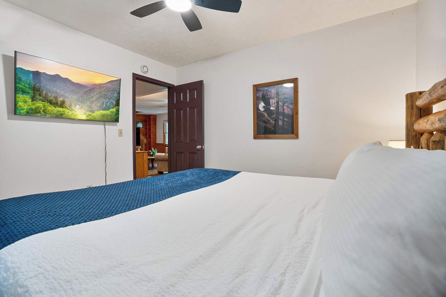 Ein Schlafzimmer mit einem Bett, einem Deckenventilator, einem Gemälde und einer Tür zu einem anderen Raum.