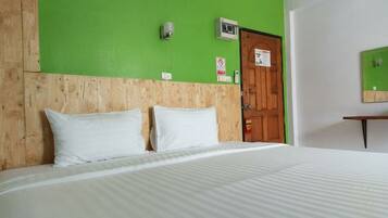 A hotel room with a wooden headboard, a bed with white bedding, a green wall, a wooden door, and a small table with a mirror.