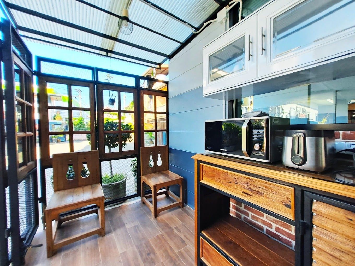 A compact kitchen with a microwave, toaster, and cabinet, a wooden bench, and a glass door leading to an outdoor area.