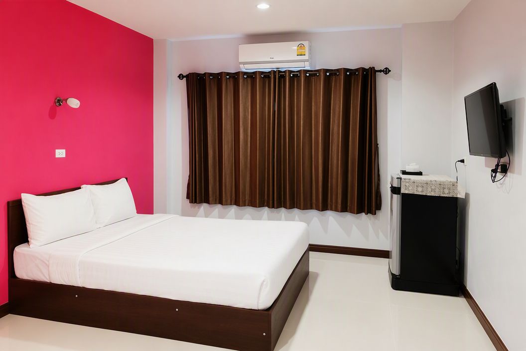 Una habitación de hotel con una cama, un aire acondicionado, un televisor y una ventana con cortinas.