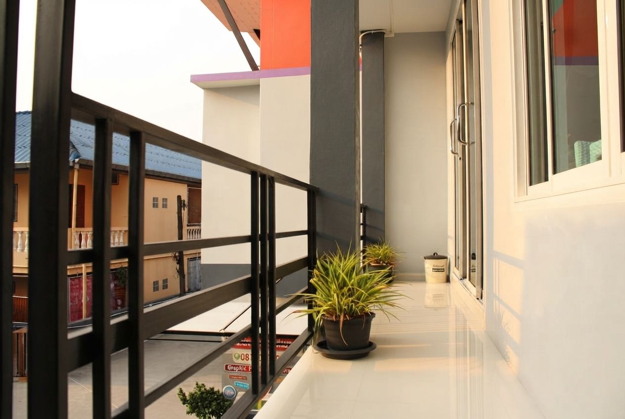 A balcony with a black metal railing, a potted plant, and a small trash bin.