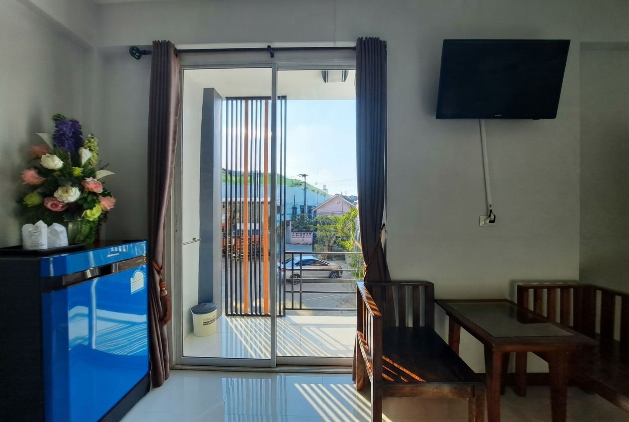 A room with a sliding glass door leading to a balcony, a television mounted on the wall, a blue cabinet, and a wooden bench.