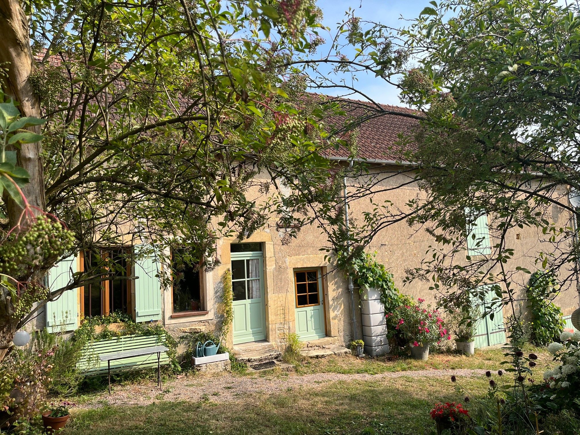 Une maison de campagne avec un jardin, un banc et un chemin menant à l’entrée.