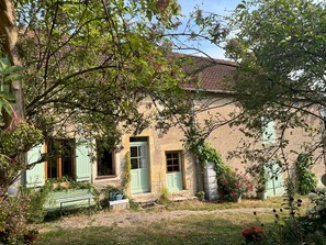 A rustic house with a garden, a bench, and a pathway leading to the entrance.