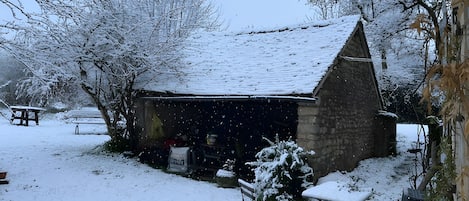 Un espace extérieur enneigé avec un bâtiment en pierre, un banc et une petite table.