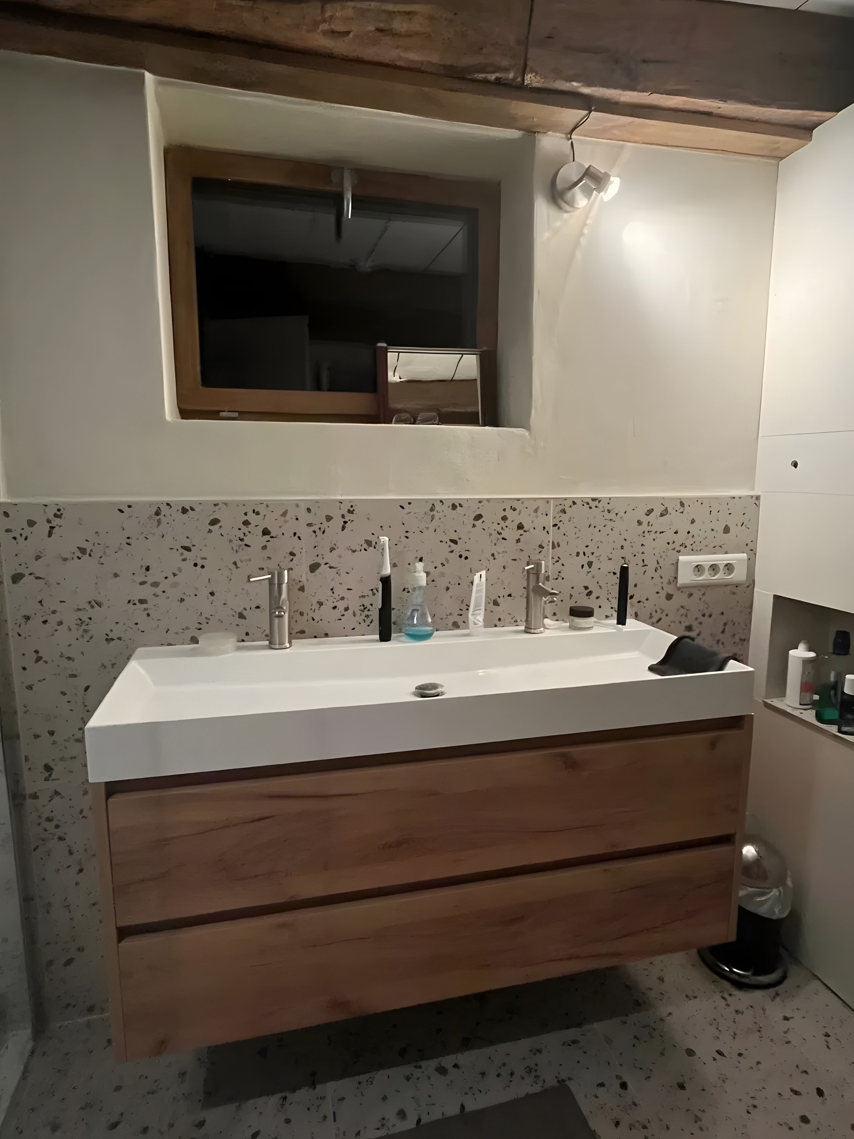 Une salle de bain avec un lavabo blanc, un meuble-lavabo en bois et un miroir au-dessus.