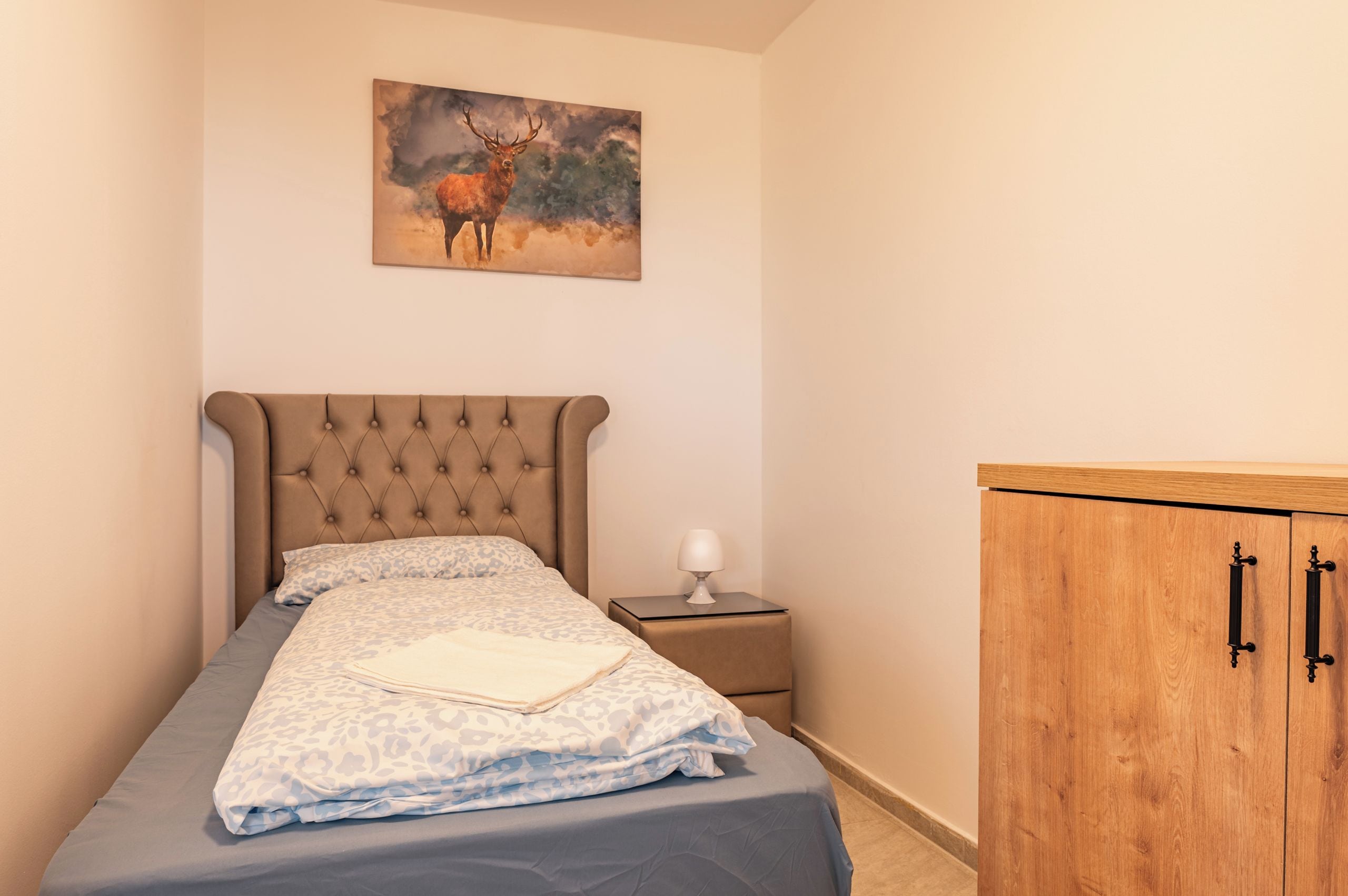 A bedroom with a bed, a nightstand, a lamp, and a wooden wardrobe.