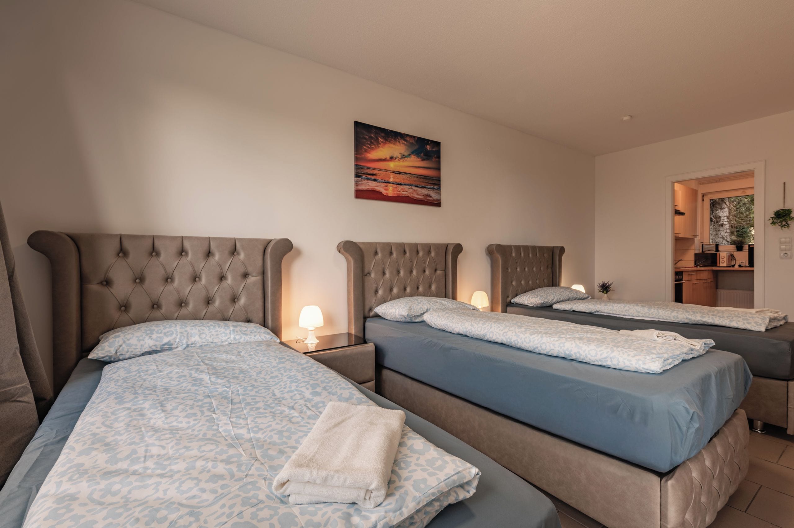 A hotel room with three beds, each with a headboard and a bedside lamp.