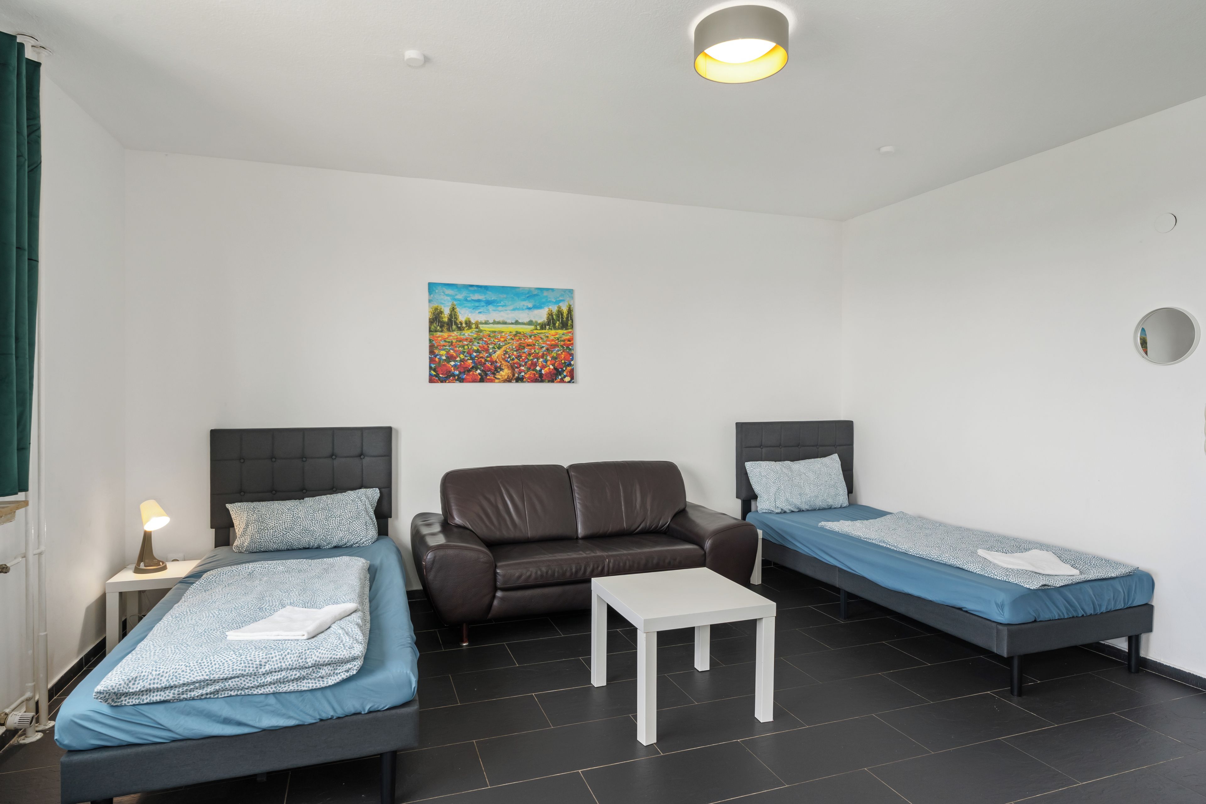 A room with two beds, a sofa, a small table, and a painting on the wall.