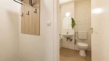 Un baño con pared de paneles de madera, un lavabo blanco, un espejo, un inodoro y una planta colgante.