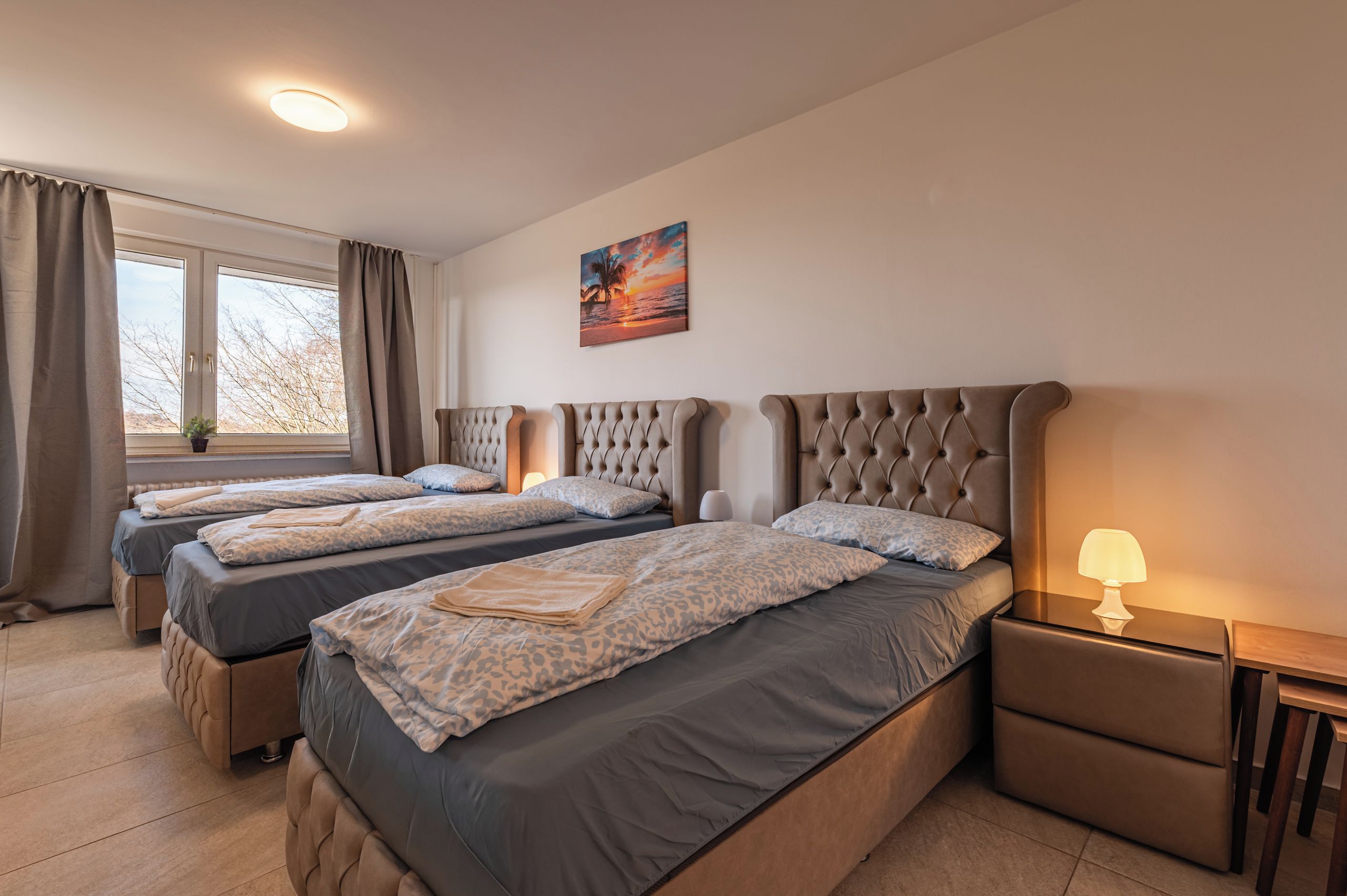 Habitación de hotel con dos camas, una ventana con cortinas, un cuadro en la pared y una lámpara de noche.