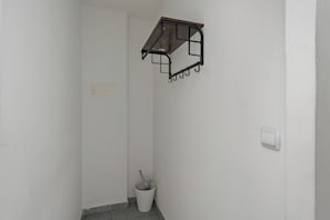A corner of a room with a white wall, a metal rack with hooks, a white bucket with a cleaning tool, and a light switch.