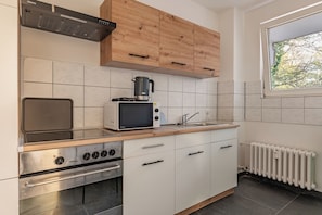 A modern kitchen with a built-in oven, microwave, and kettle, wooden cabinets, and a window with a view.