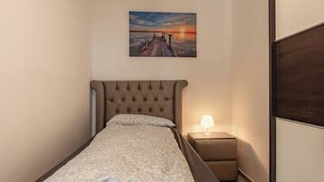 Una cama individual con cabecera, una mesita de noche con lámpara, y un cuadro colgado en la pared que muestra un atardecer sobre un muelle.