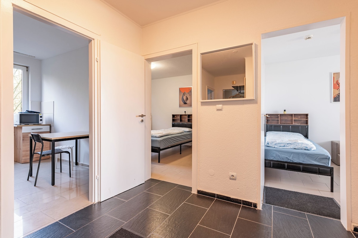 Habitació petita amb llit, escriptori i cadira, amb vista a una altra habitació.