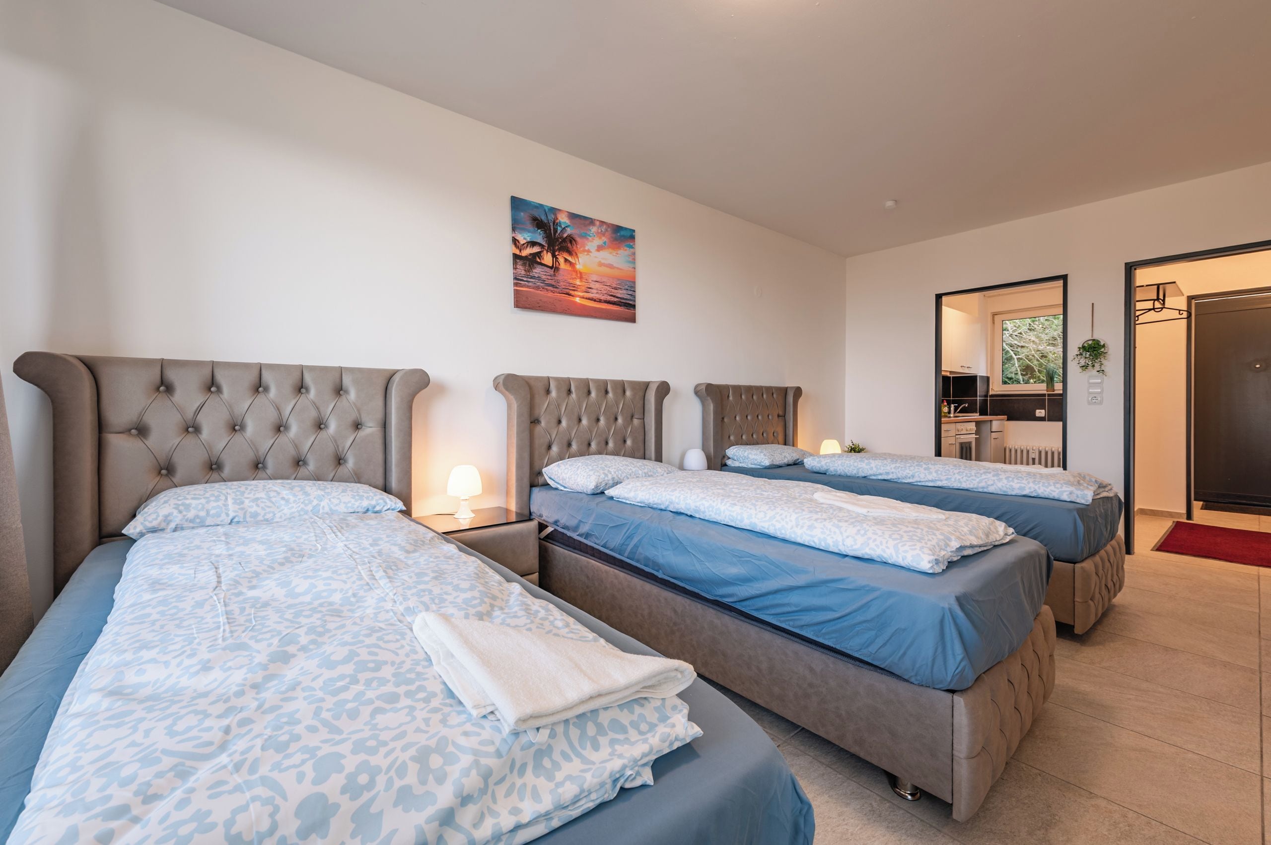 A hotel room with two beds, a painting on the wall, and a view of the outside.
