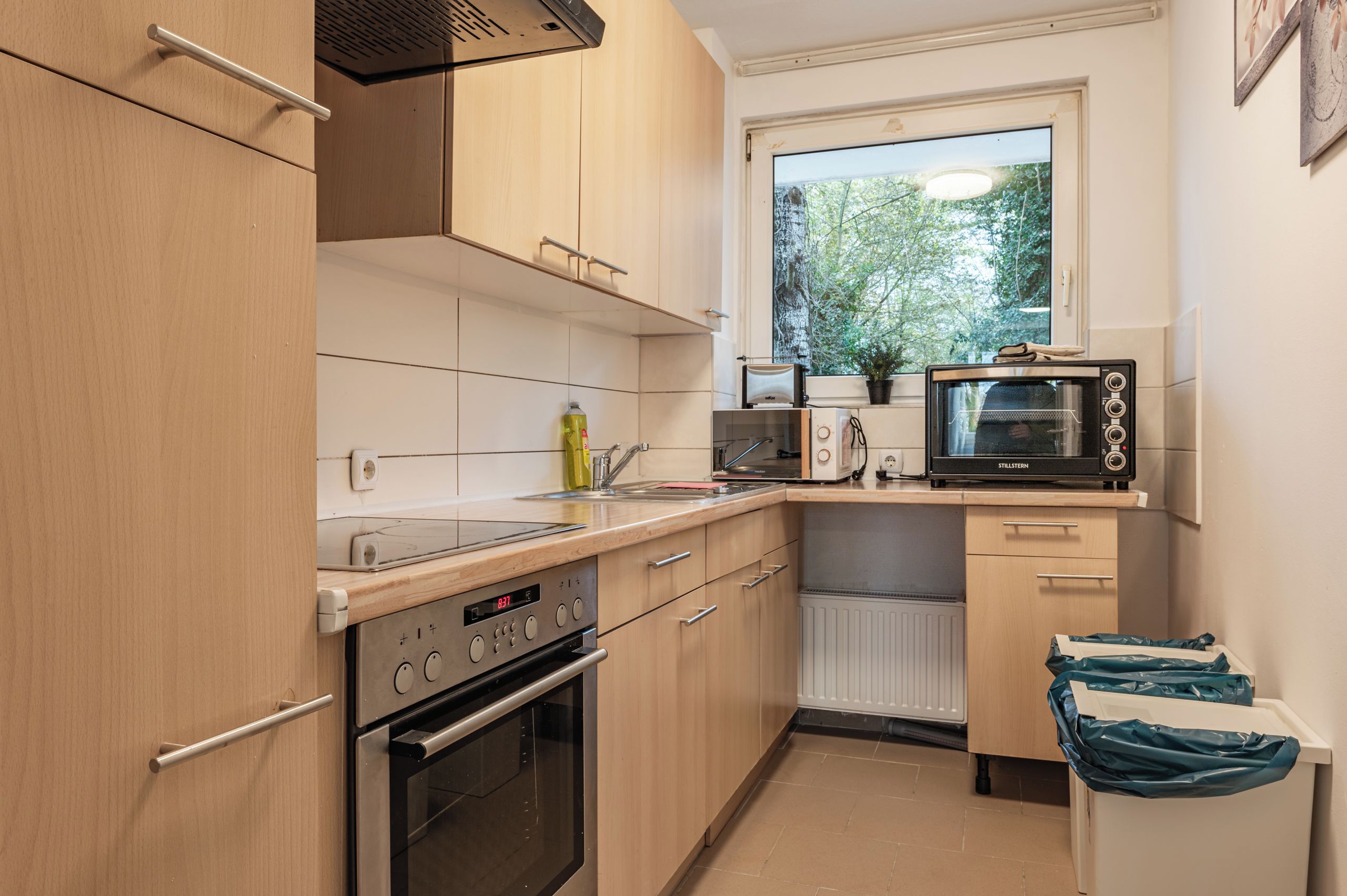 A compact kitchen with a built-in oven, microwave, and a window above the sink.
