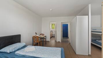 Quarto com cama, escrivaninha e cozinha compacta.