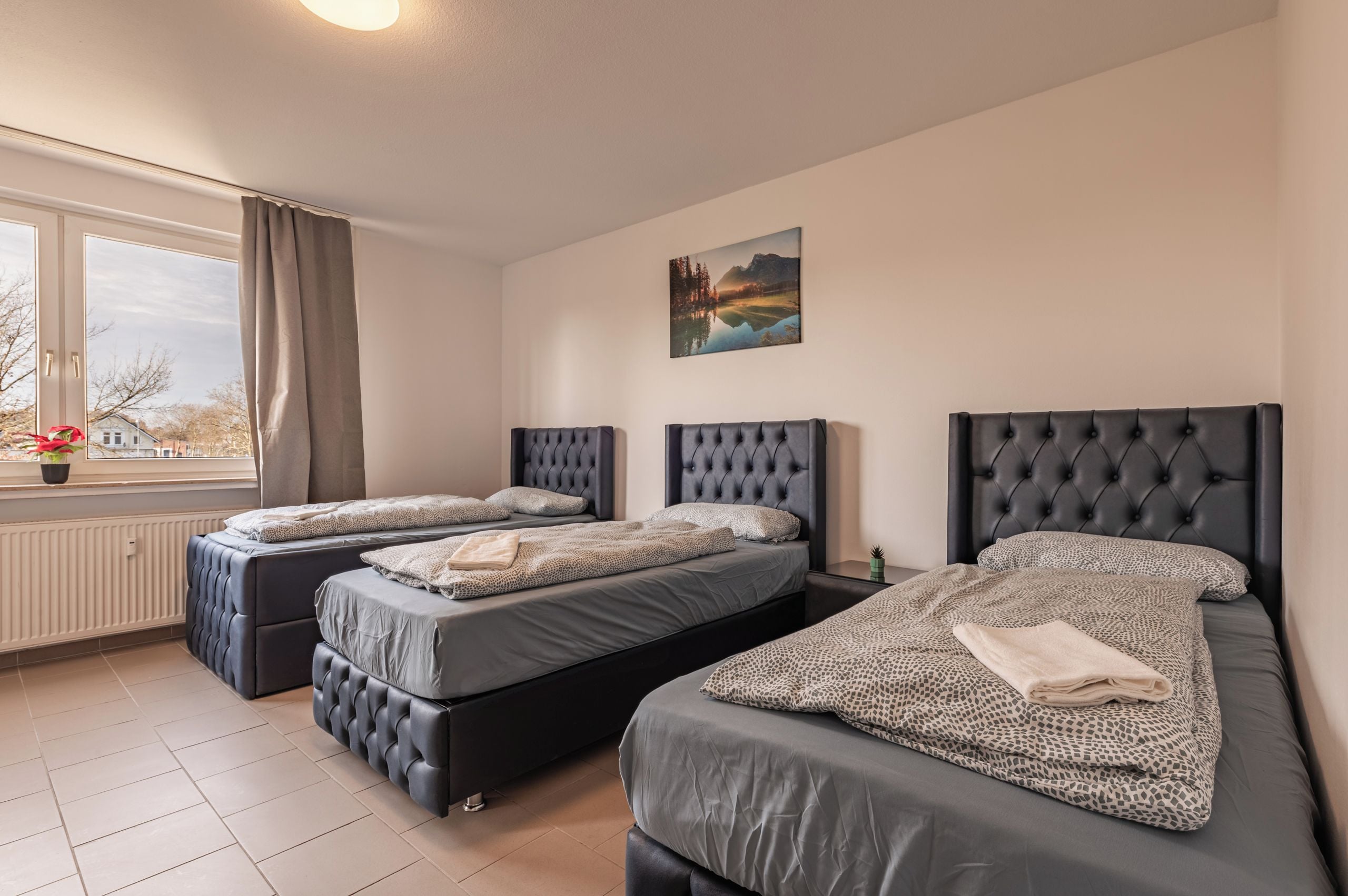 Habitación de hotel con dos camas, una ventana con cortinas, un radiador y un cuadro en la pared.