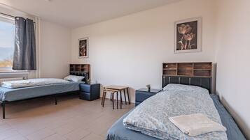 A bedroom with two beds, a small table, and a window with curtains.