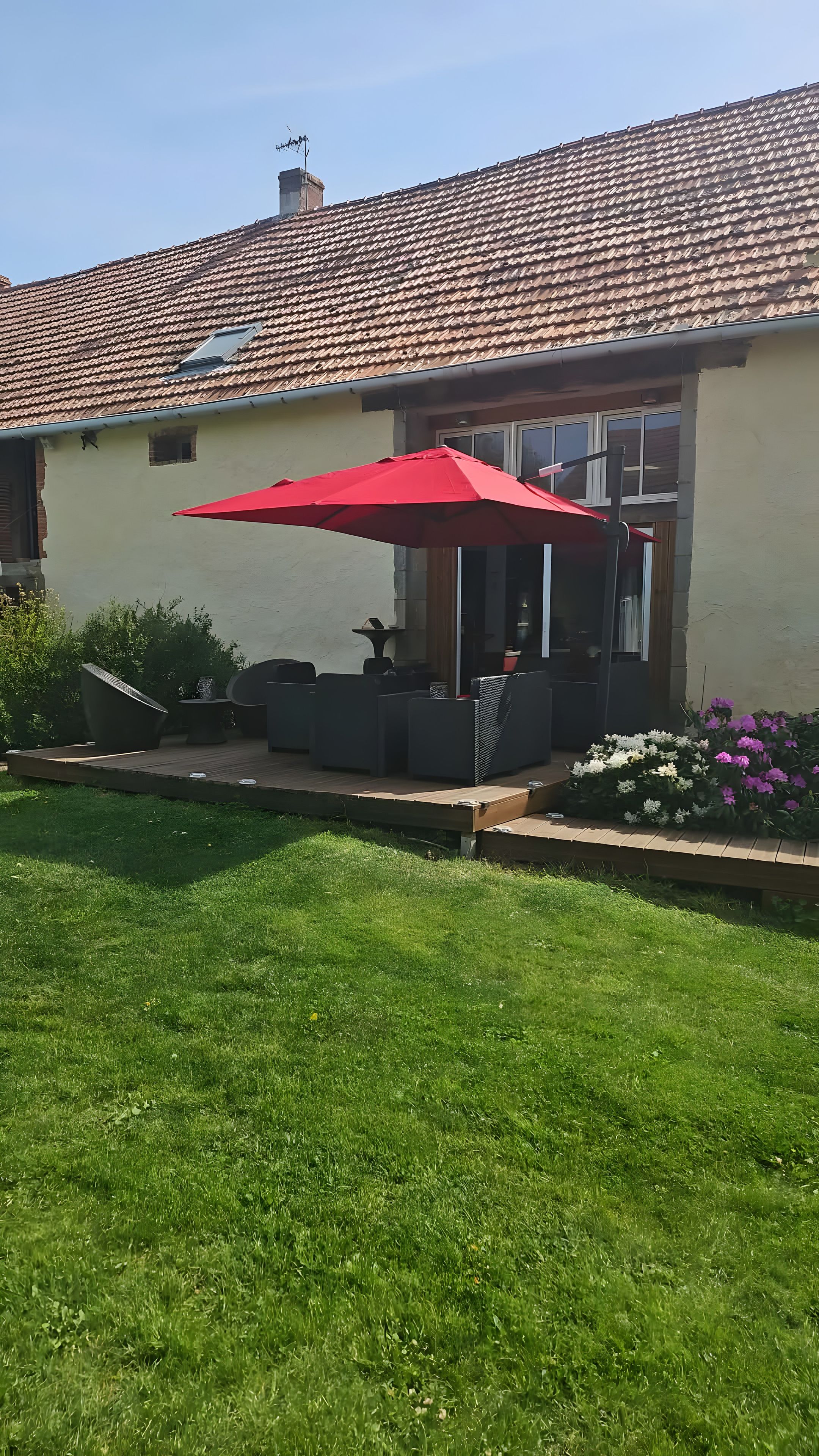 A house with a tiled roof, a patio with outdoor furniture, and a red umbrella.