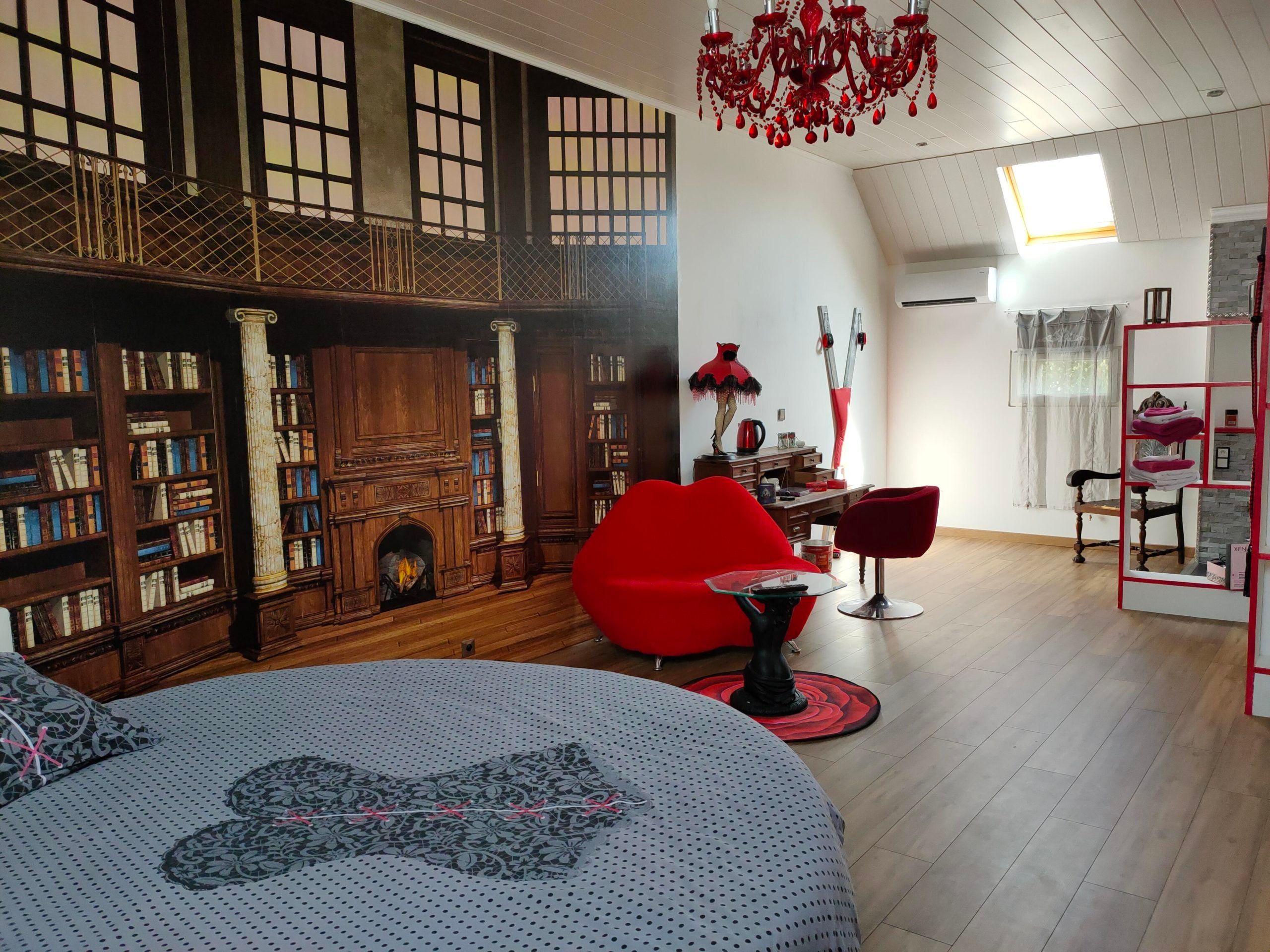 Une pièce avec une cheminée, des étagères à livres, un fauteuil rouge et une lampe moderne.