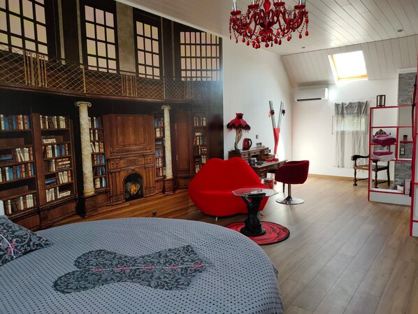 A room with a fireplace, bookshelves, a red chair, and a modern lamp.