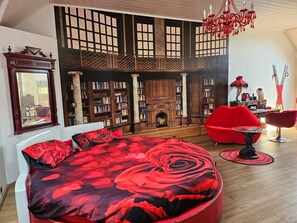 Una habitación con una cama grande, un sillón rojo, un sofá rojo, una chimenea y una estantería.