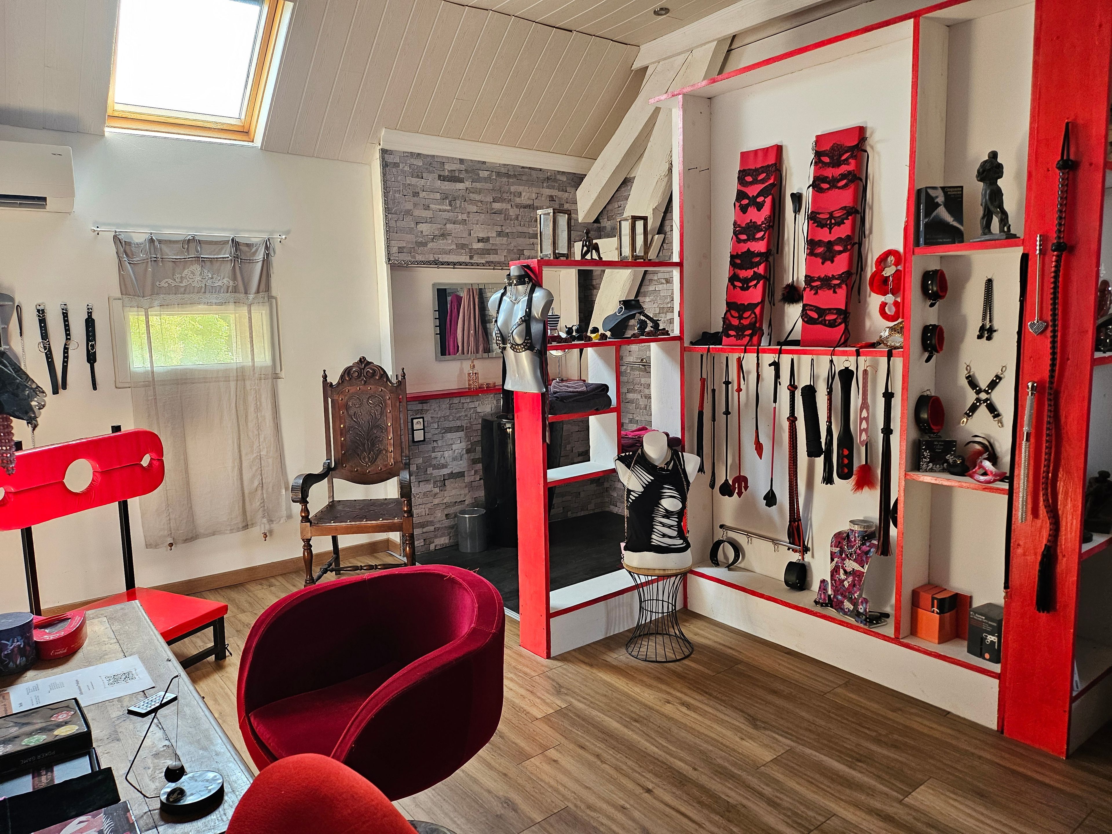 Une pièce comprenant une chaise rouge, une table en bois avec divers objets, un mannequin et un mur orné de différents éléments.
