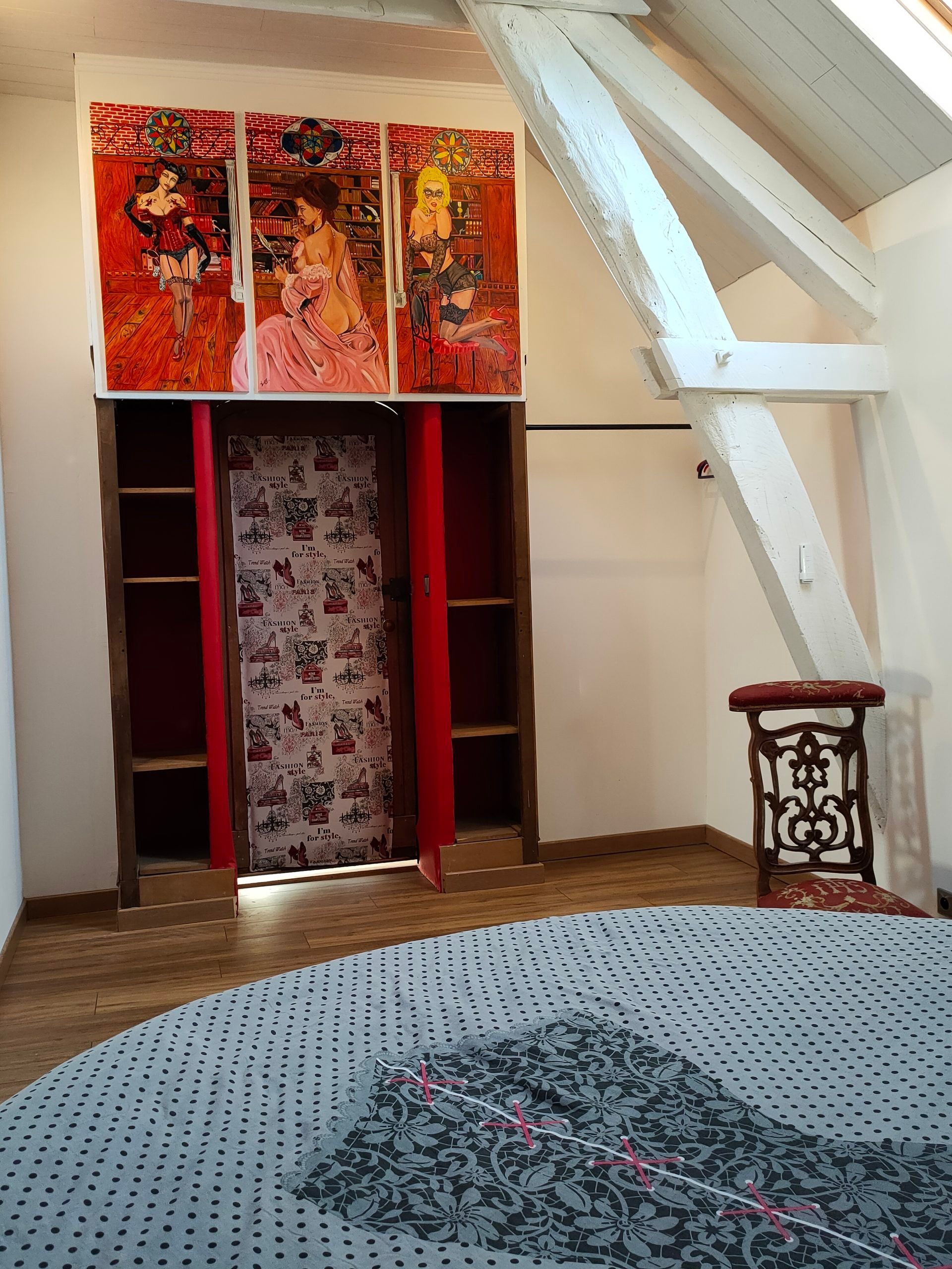 Ein Zimmer mit Holzboden, einem gemusterten Teppich, einem roten Vorhang und einer Wand mit einem dreiteiligen Kunstwerk.