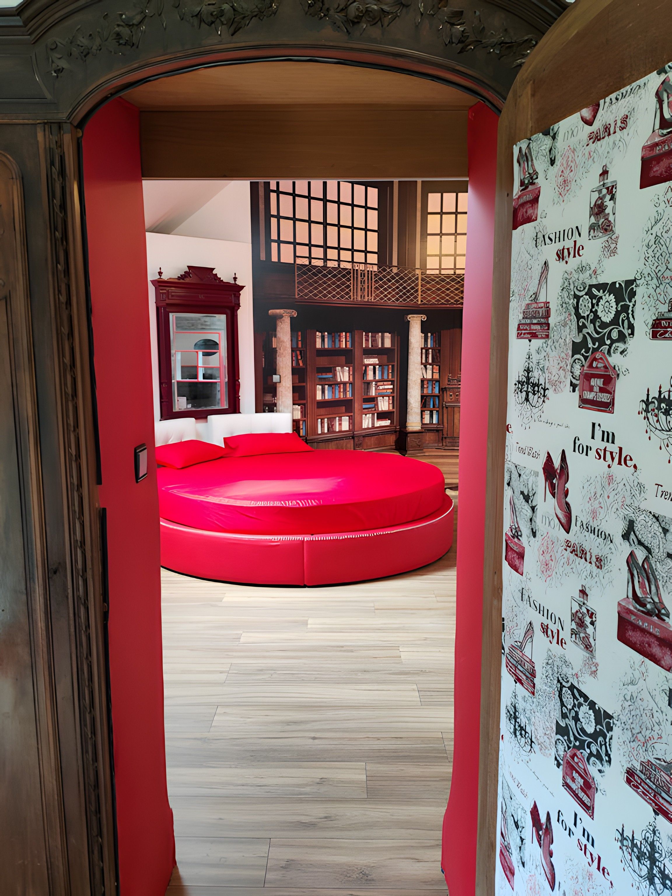 A room with a red circular bed, wooden bookshelves, and a large mirror.