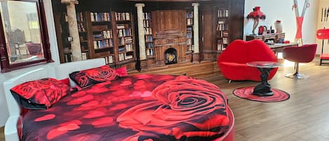 Una sala de estar moderna con un sofá rojo grande, un sillón rojo, una mesita redonda pequeña y una estantería llena de libros.