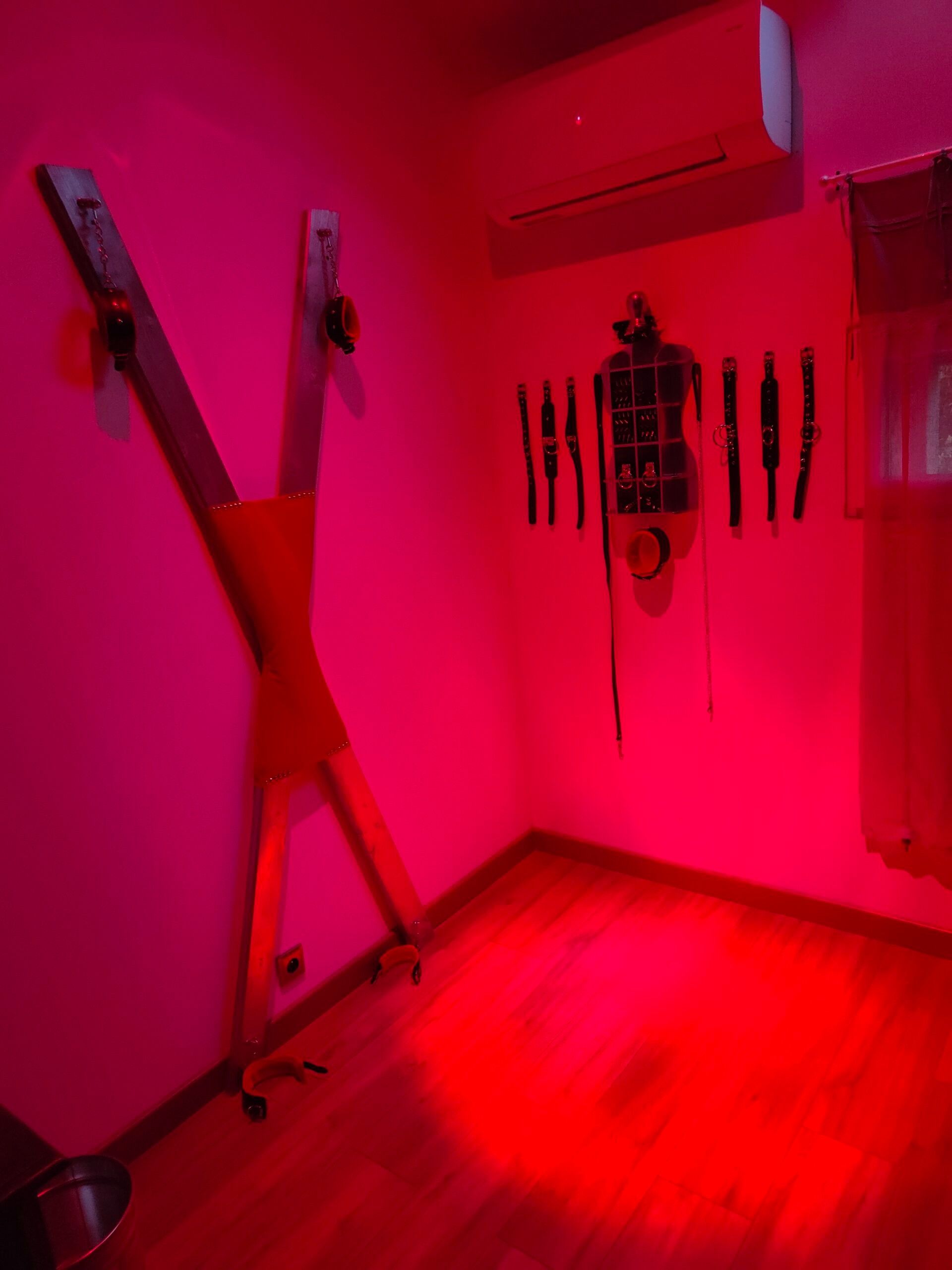 A room with a wooden floor, a wall-mounted air conditioning unit, and a collection of belts and straps hanging on the wall.