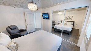Une chambre avec un grand lit, une chaise, une télévision et un miroir.