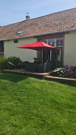 Ein Haus mit einem Ziegeldach, einer Terrasse mit Gartenmöbeln und einem roten Sonnenschirm.