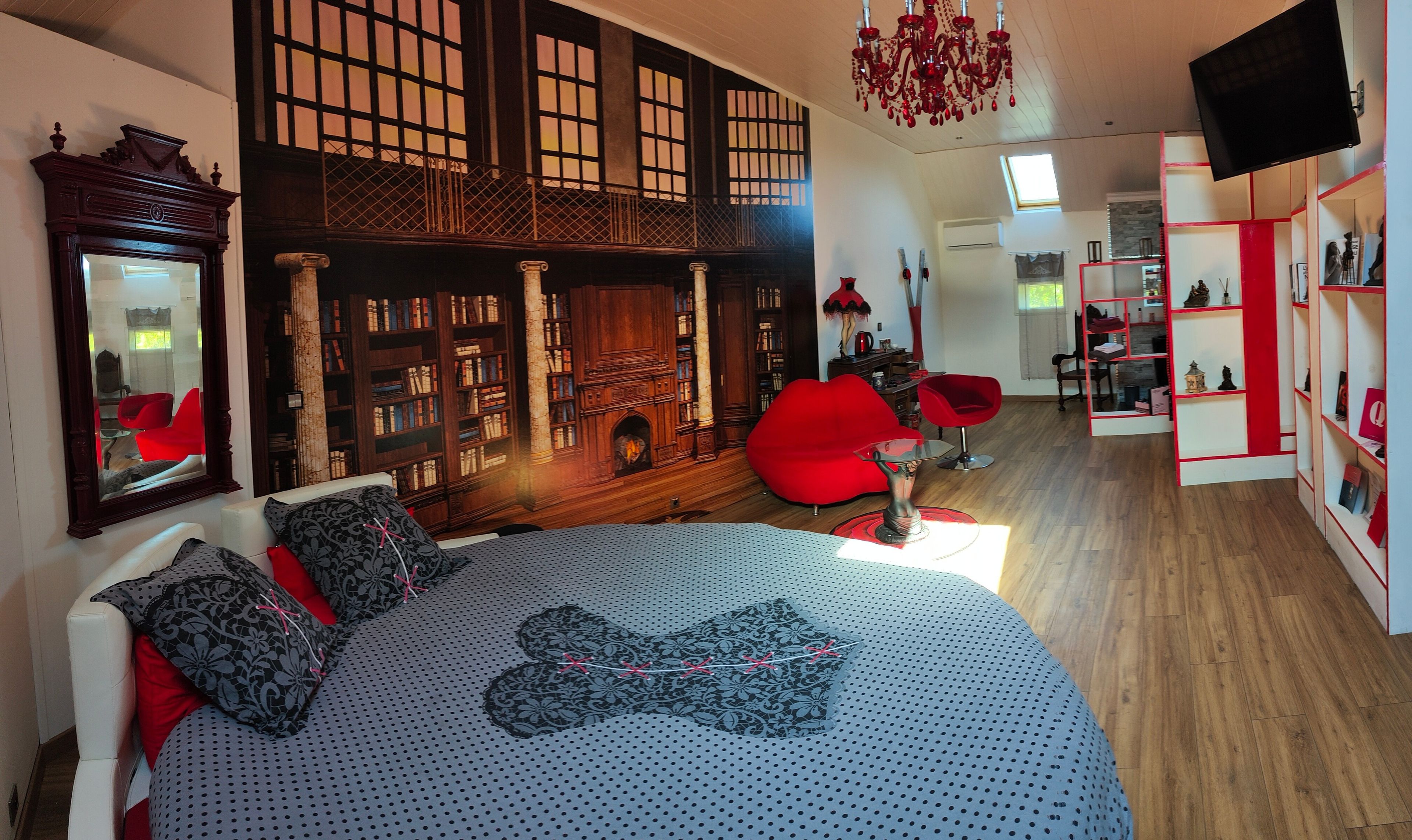Un dormitorio con una cama grande, una silla roja, una estantería y un televisor.